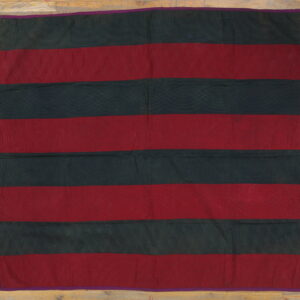A flat, striped textile in maroon and dark green has intricate quilted stitching and a narrow purple border.