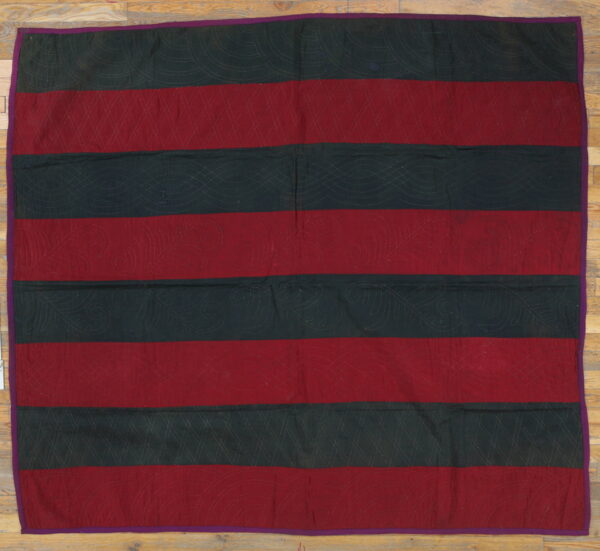 A flat, striped textile in maroon and dark green has intricate quilted stitching and a narrow purple border.