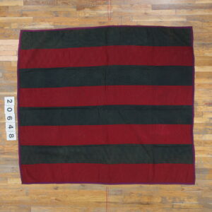 Red and dark green striped flat textile with quilted stitching patterns rests on light wood floorboards.