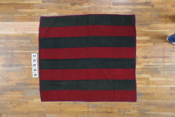 Red and dark green striped flat textile with quilted stitching patterns rests on light wood floorboards.