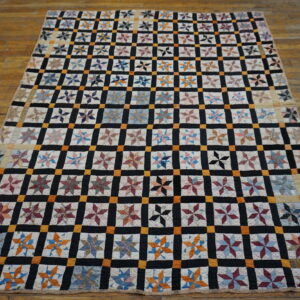 Black, orange, and white grid patchwork quilt with multicolored star blocks on a distressed wood floor.