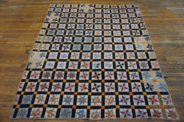 Black, orange, and white grid patchwork quilt with multicolored star blocks on a distressed wood floor.