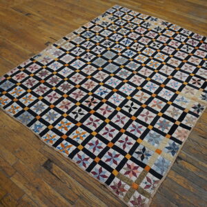 Colorful star patchwork rug with a black and gold grid pattern lies flat on a distressed wood floor.