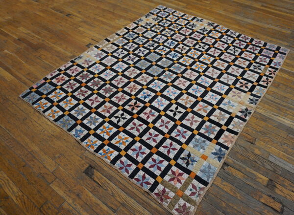 Colorful star patchwork rug with a black and gold grid pattern lies flat on a distressed wood floor.