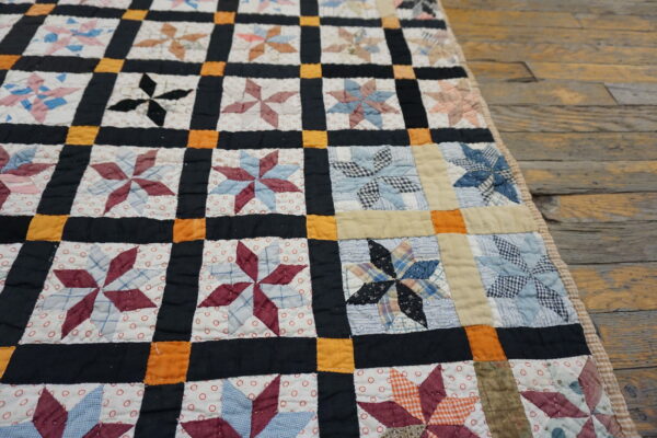 Quilted patchwork textile with multi-colored pinwheel stars framed by black and orange strips on rustic wood planks.