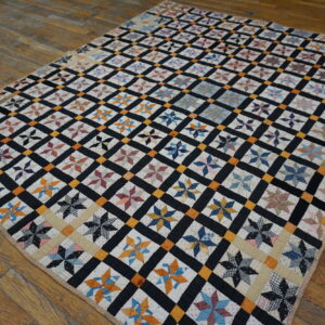 Multicolor star quilt blocks are framed by a black and orange grid, lying on rustic wood floors.