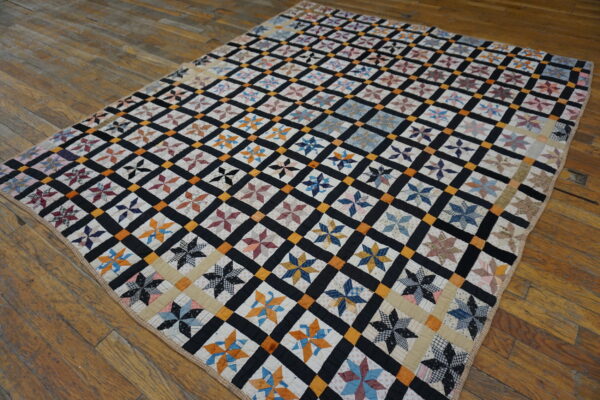 Multicolor star quilt blocks are framed by a black and orange grid, lying on rustic wood floors.