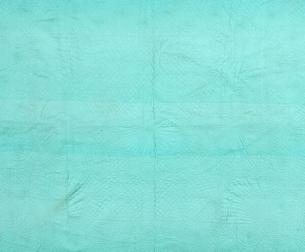 Light turquoise rug featuring an embossed texture of circular and radial quilted designs across the wrinkled surface.