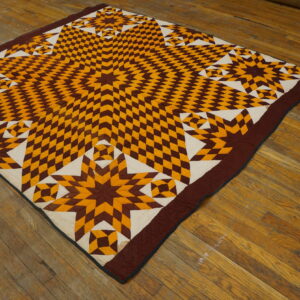 Brown, gold, and cream geometric star quilt laid flat on a distressed plank wood floor.