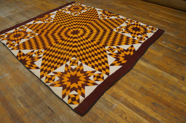 Brown, gold, and cream geometric star quilt laid flat on a distressed plank wood floor.