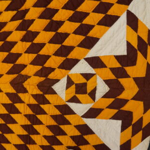 Brown, amber, and white quilted textile with geometric shapes rests partially on worn, distressed wood flooring.