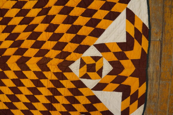 Brown, amber, and white quilted textile with geometric shapes rests partially on worn, distressed wood flooring.