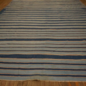 Wide flatweave rug with dark and light blue horizontal stripes accented by thin orange lines on a wood floor.