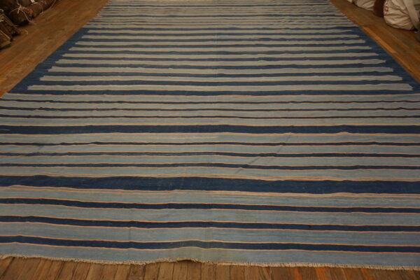 Wide flatweave rug with dark and light blue horizontal stripes accented by thin orange lines on a wood floor.