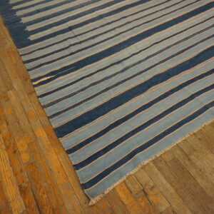 A flatweave rug with navy and light blue stripes, separated by thin orange lines, rests on distressed wood flooring.