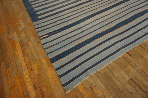 A flatweave rug with navy and light blue stripes, separated by thin orange lines, rests on distressed wood flooring.