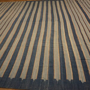Dark blue and muted gray striped flatweave rug featuring thin orange accents on a wood floor.