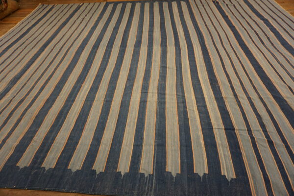 Dark blue and muted gray striped flatweave rug featuring thin orange accents on a wood floor.