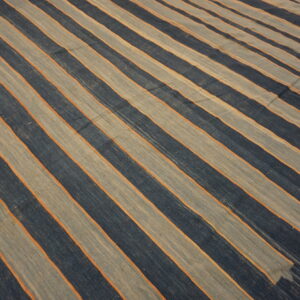 A low-pile rug featuring wide diagonal indigo and light gray stripes separated by thin orange lines.