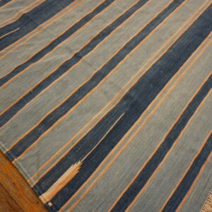 Flatweave striped rug in varying shades of blue and orange lines rests on distressed hardwood.