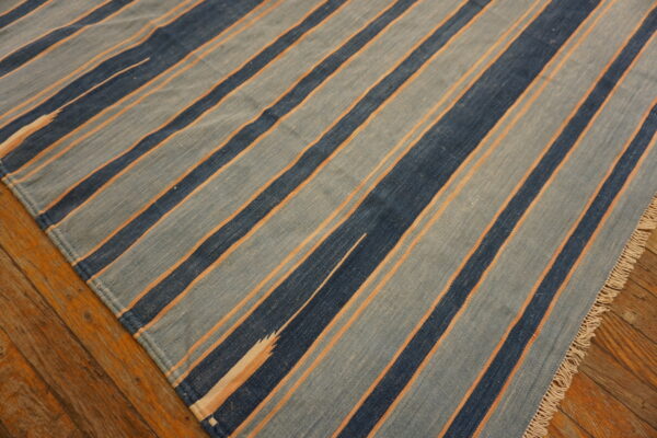 Flatweave striped rug in varying shades of blue and orange lines rests on distressed hardwood.