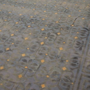 Muted blue and gray rug with gold diamonds, floral motifs, and a Greek key border on wood floor.