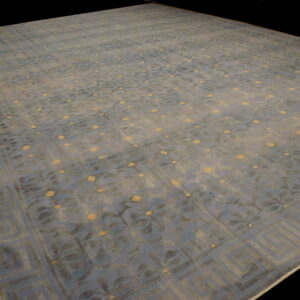 Low-pile blue rug featuring repeating floral designs, gold spots, and a wide geometric key border.