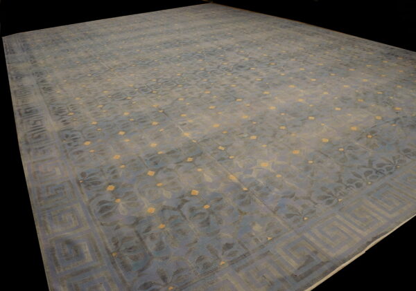 Low-pile blue rug featuring repeating floral designs, gold spots, and a wide geometric key border.