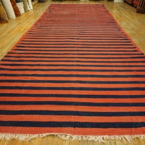 Long flatweave rug featuring wide horizontal stripes of rust red and navy blue on a wood floor.