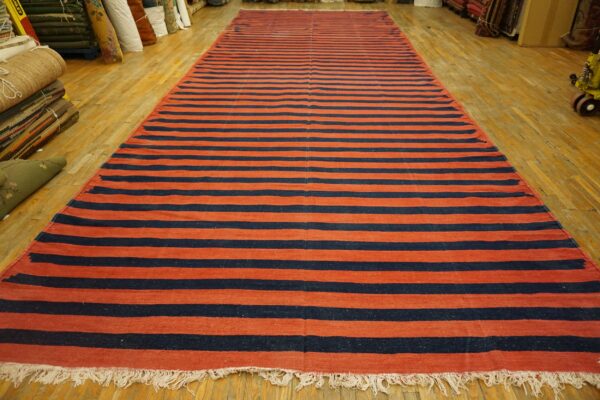 Long flatweave rug featuring wide horizontal stripes of rust red and navy blue on a wood floor.