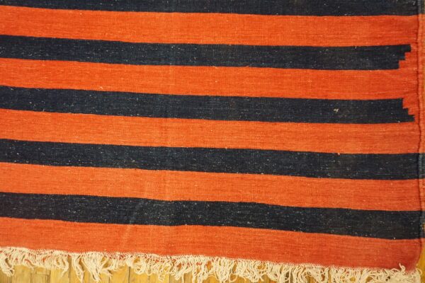 Orange and dark striped flatweave rug with white fringe resting on a light wood floor.