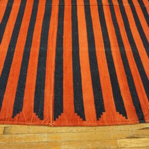 A flatweave rug with alternating rust and navy vertical stripes lies on distressed wood floors.