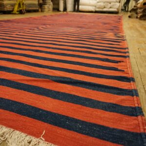 Long flatweave rug featuring alternating rust-colored and navy stripes rests on wood flooring.