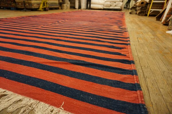 Long flatweave rug featuring alternating rust-colored and navy stripes rests on wood flooring.