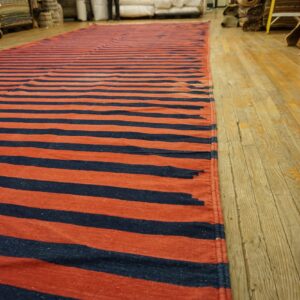 Long flatweave rug featuring wide horizontal navy and rust stripes on aged wood flooring.