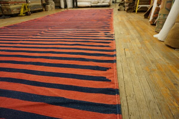 Long flatweave rug featuring wide horizontal navy and rust stripes on aged wood flooring.