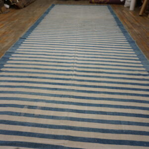 Long blue and cream striped flatweave rug displayed on rustic wooden flooring.