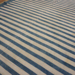 Flatwoven rug featuring wide blue and cream stripes and a decorative pointed edge on a wooden floor.