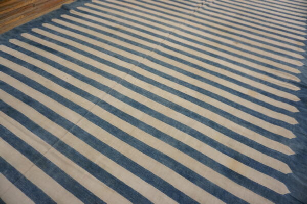 Flatwoven rug featuring wide blue and cream stripes and a decorative pointed edge on a wooden floor.