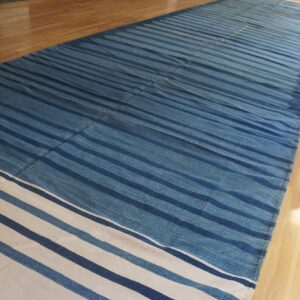 Striped blue and cream flatweave rug on a light wood floor with bright window light.