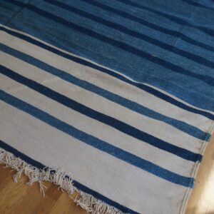 A flat-weave rug featuring white, navy, and denim blue horizontal stripes and fringe on hardwood flooring.