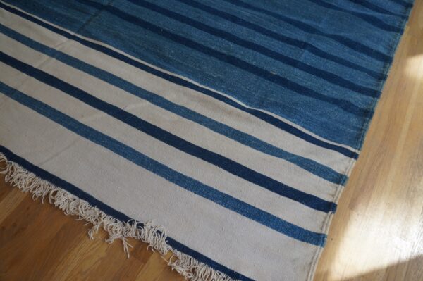 A flat-weave rug featuring white, navy, and denim blue horizontal stripes and fringe on hardwood flooring.