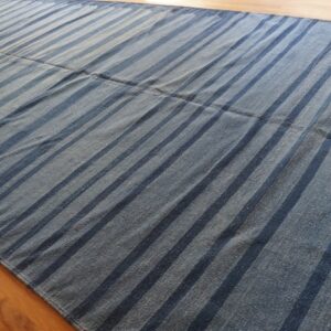 Low-pile blue rug with wide dark indigo stripes displayed flat on light hardwood flooring.