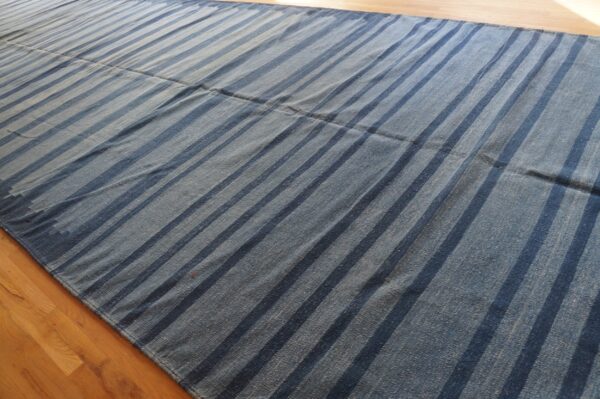 Low-pile blue rug with wide dark indigo stripes displayed flat on light hardwood flooring.