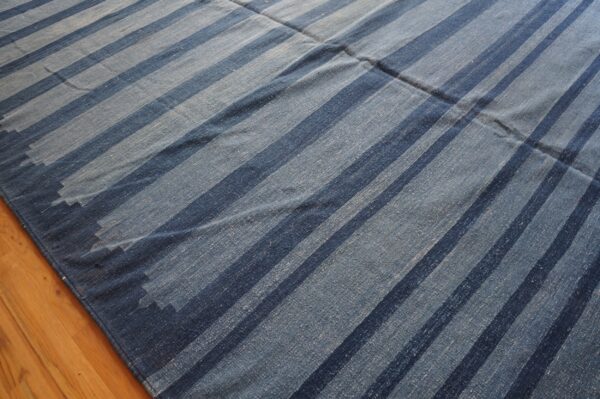 Blue flatweave rug features wide vertical stripes of dark and light denim blue on hardwood floor.