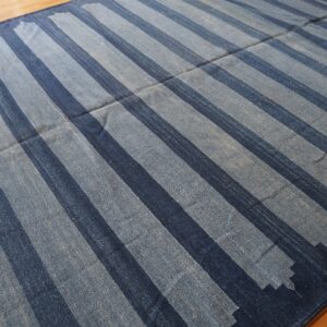 Blue flatweave rug featuring wide stripes with jagged edges on a wooden floor.