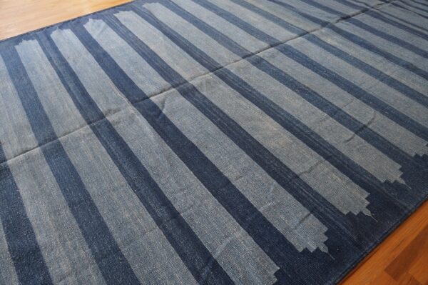 Blue flatweave rug featuring wide stripes with jagged edges on a wooden floor.