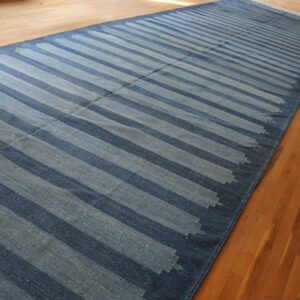 A long, narrow blue flatweave runner with thick diagonal stripes lies on warm-toned hardwood flooring.