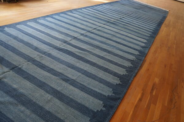 A long, narrow blue flatweave runner with thick diagonal stripes lies on warm-toned hardwood flooring.