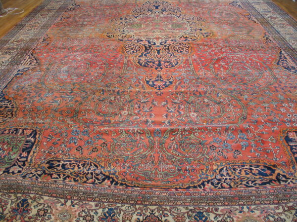 Large traditional rug featuring faded red and navy floral patterns and a medallion on wood flooring.